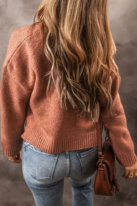 Person wearing a brown sweater and blue jeans with a brown handbag on a neutral background