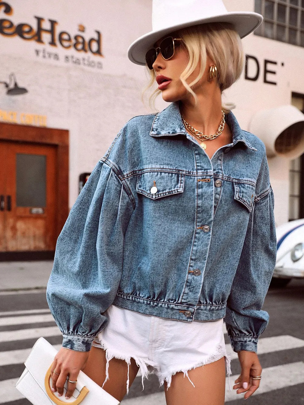 Woman wearing a denim jacket and white hat on a city street.