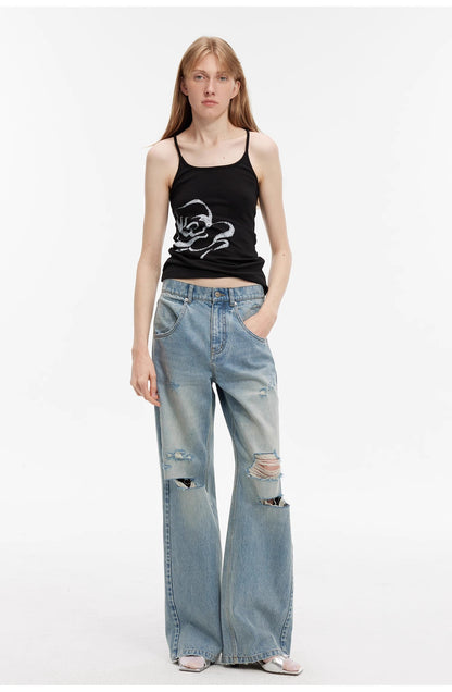 Woman wearing a black tank top with a graphic design and light blue ripped jeans on a white background