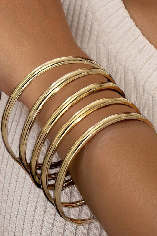 Gold bangles on a wrist with a neutral background