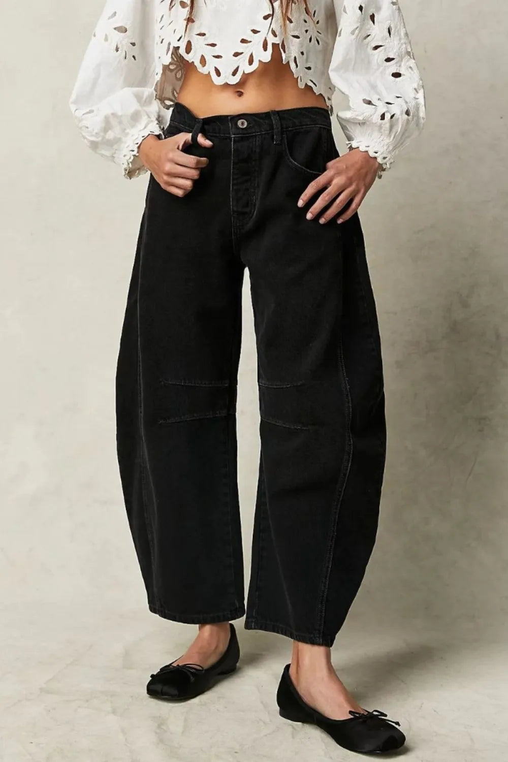 Person wearing a white blouse with black polka dots and black wide-leg pants on a neutral background
