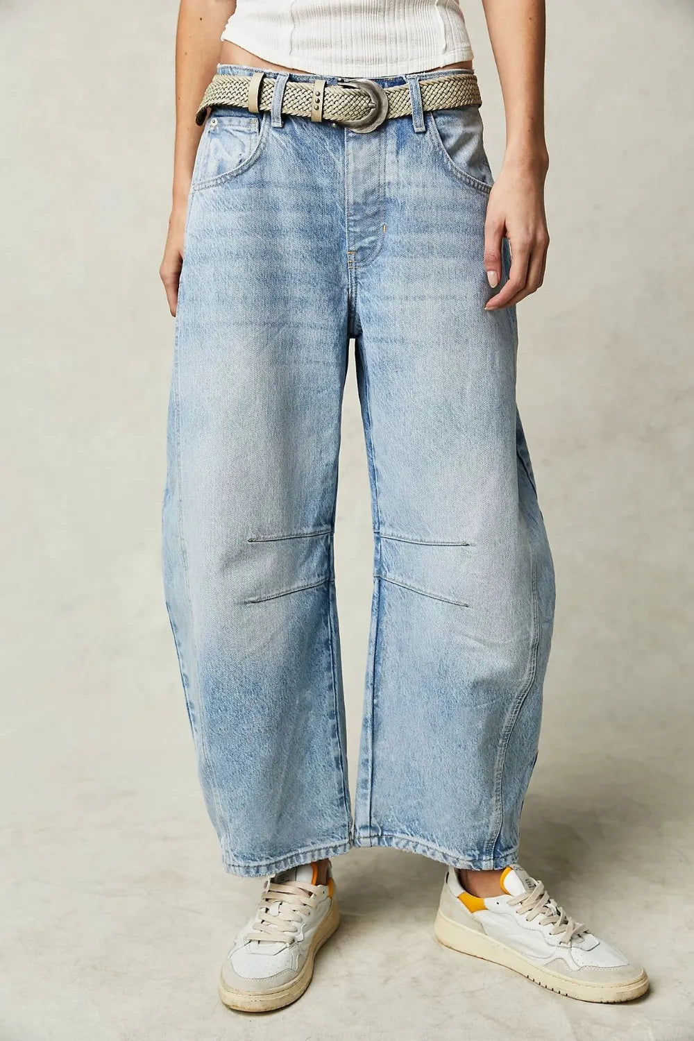 Person wearing light blue wide-leg jeans with a belt on a neutral background