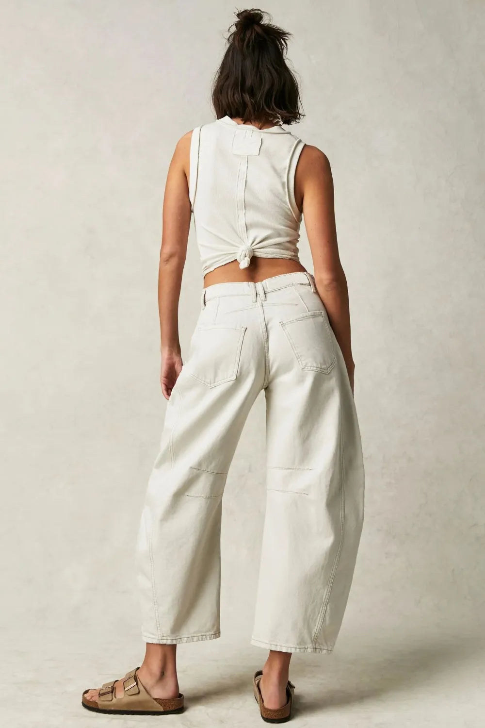 Person wearing a white sleeveless top and wide-leg pants against a plain background