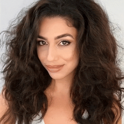 Smiling woman with long dark hair sectioned and clipped up, preparing to demonstrate how to use the beachwaver pro curling iron on camera