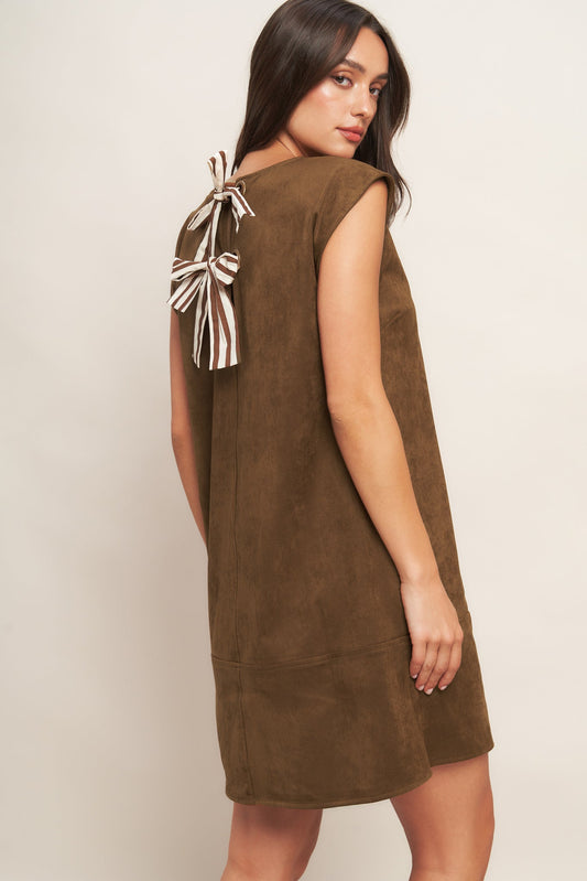 Woman wearing a brown dress with bow details on a plain background