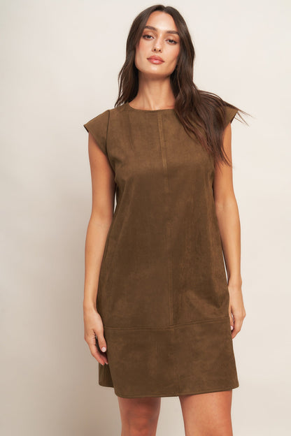 Woman wearing a brown suede dress against a plain background