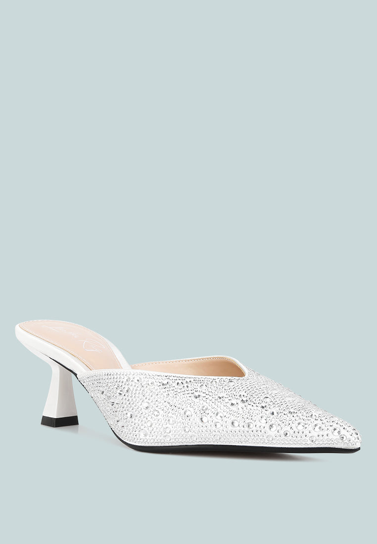 White pointed-toe mule with rhinestone embellishments on a light blue background