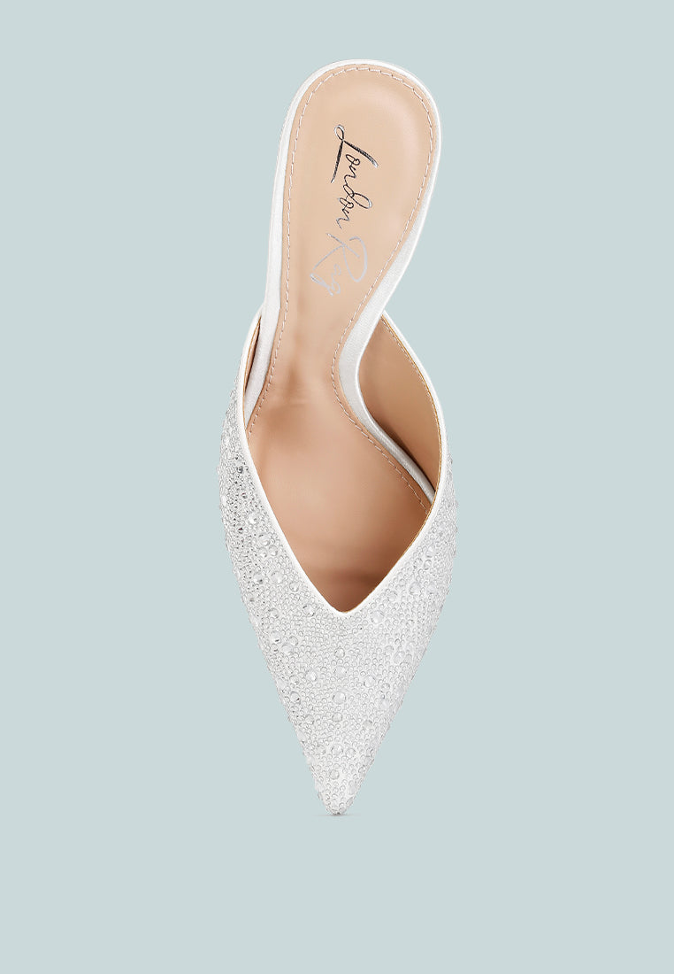 White pointed-toe shoe with embellishments on a light blue background