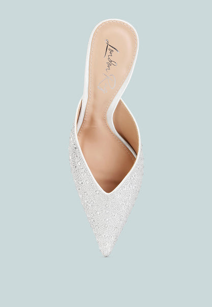 White pointed-toe shoe with embellishments on a light blue background