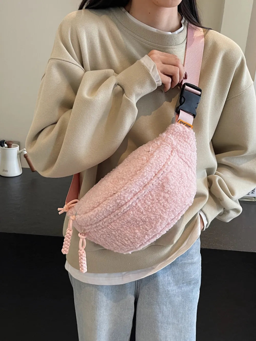 Person wearing a beige sweater and light gray pants holding a pink textured bag.
