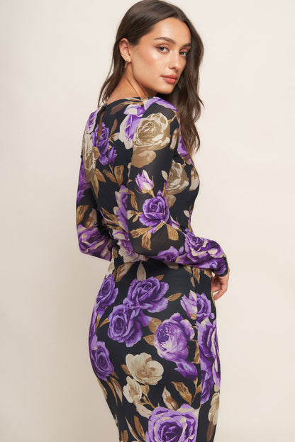 Woman wearing a floral dress with purple, gold, and black colors on a plain background