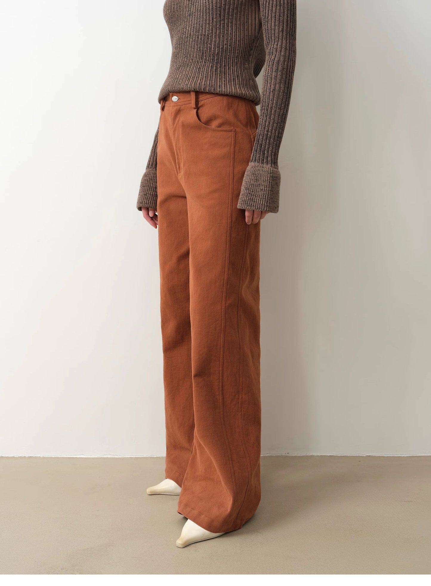Person wearing brown corduroy pants and a ribbed sweater against a plain background