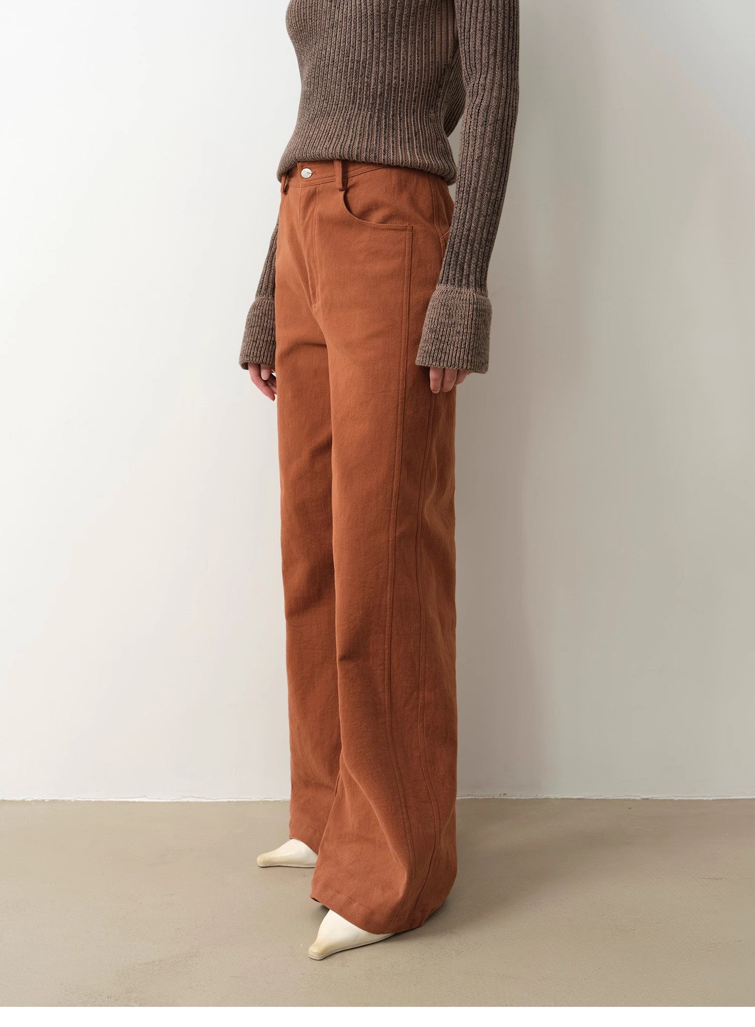 Person wearing brown corduroy pants and a ribbed sweater against a plain background