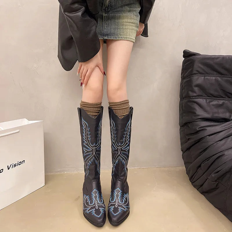 Person wearing black cowboy boots with blue designs indoors.