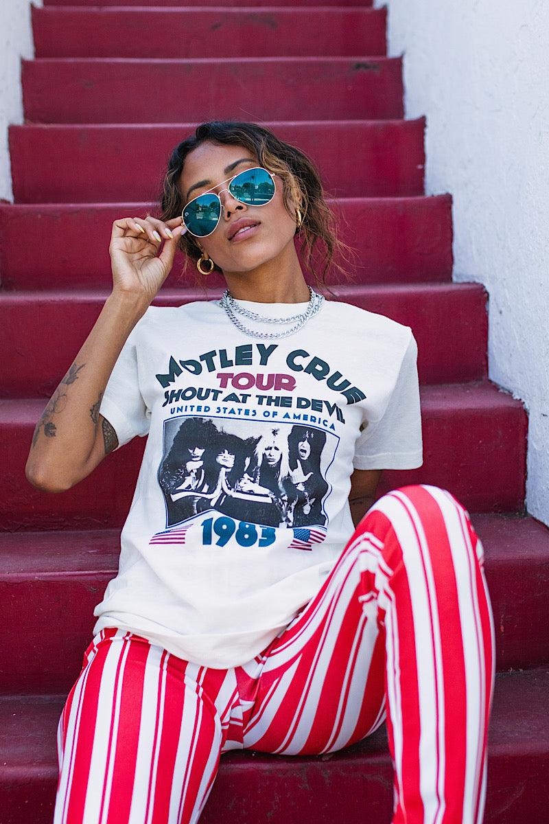 Woman wearing a Motley Crue t-shirt and red and white striped pants sitting on red steps.