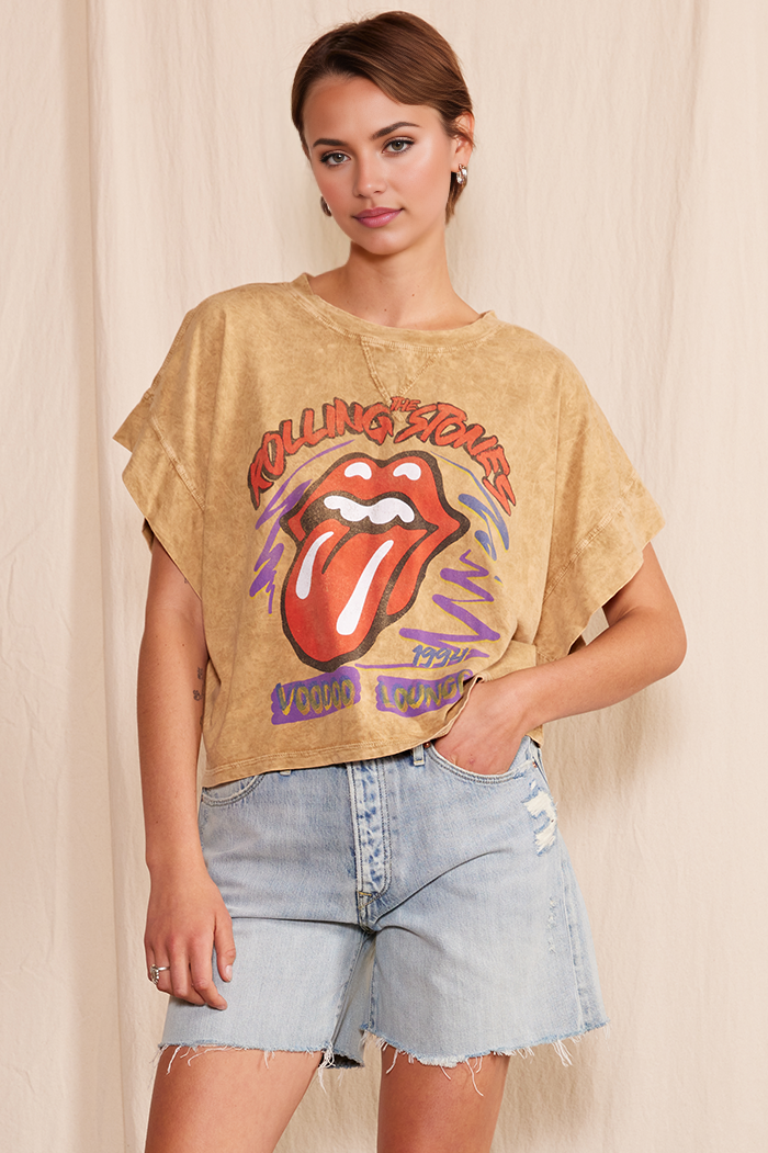 Woman wearing a Rolling Stones t-shirt and denim shorts against a beige background