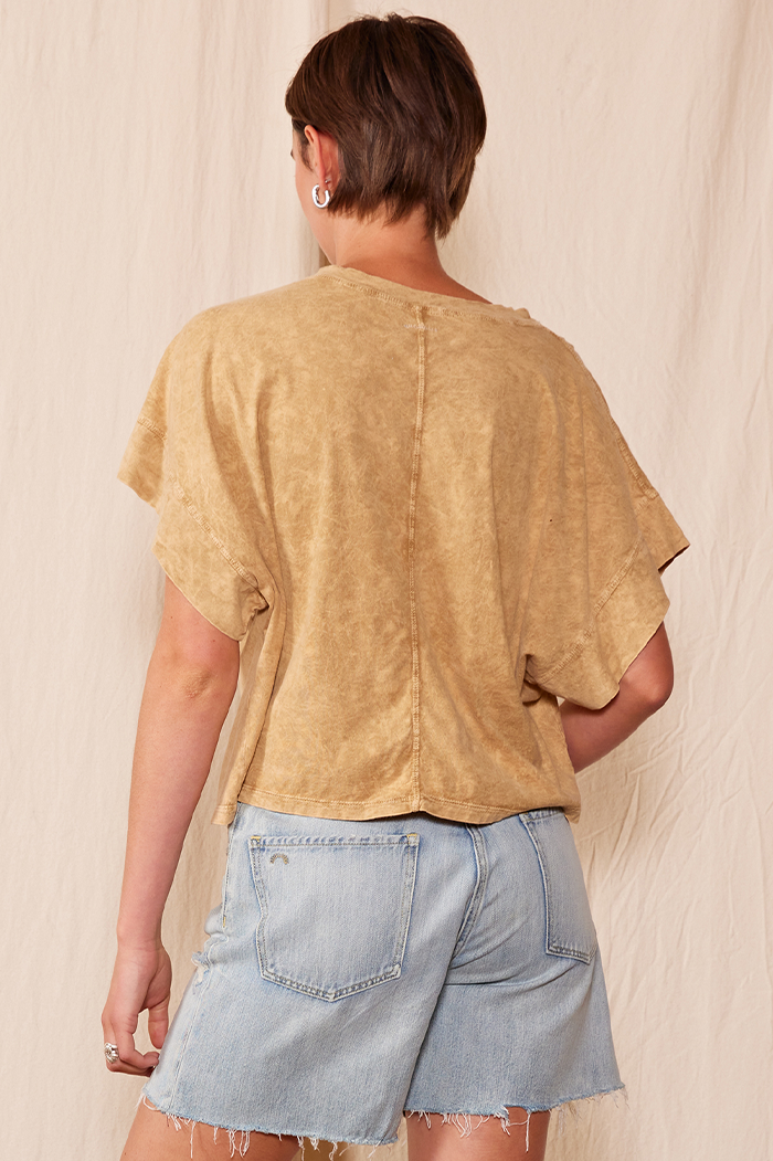 Person wearing a beige t-shirt and denim shorts against a plain background
